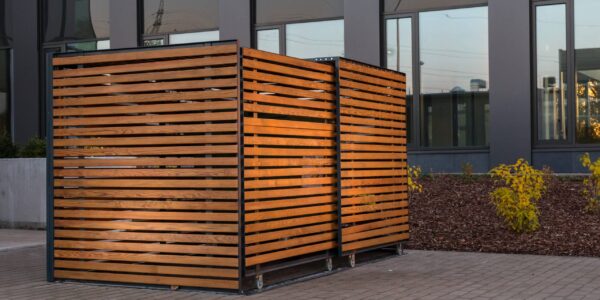 Dumpster,Containers,Hidden,Inside,Wooden,Cage,In,Front,Of,Office