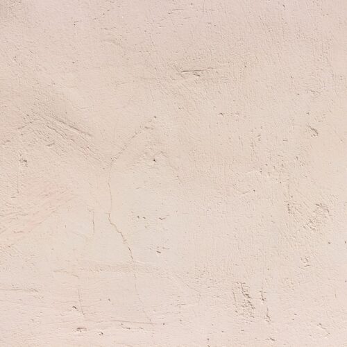 Sandfarbene Wand mit feiner, unregelmäßiger Struktur und kleinen Rissen.