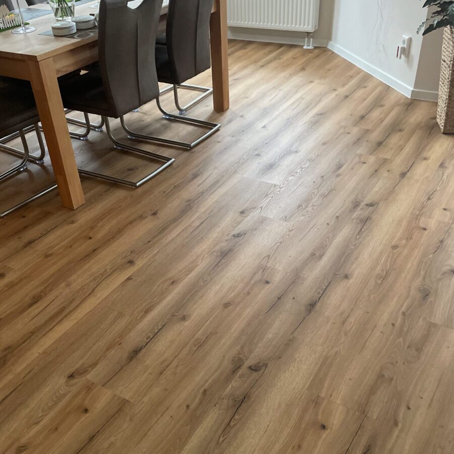 Mittelbrauner Holzboden mit sichtbarer Maserung in einem Esszimmer mit Holztisch und dunklen Stühlen.