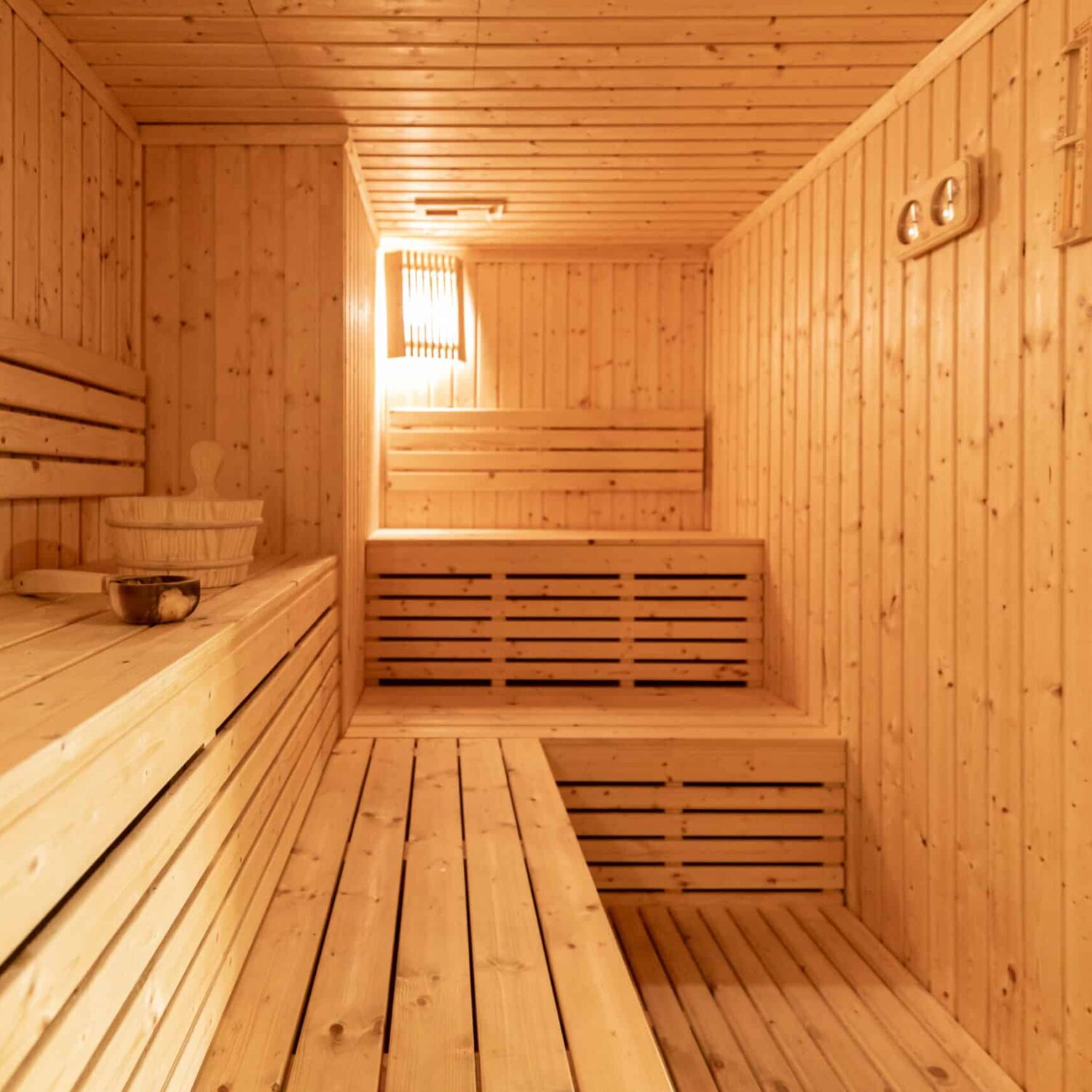 Small,Home,Wooden,Sauna,,Spa,Room.,Relax,In,A,Hot Innenraum einer Innensauna mit mehrstufigen Holzbänken, Holzwänden und einer kleinen Wandlampe.
