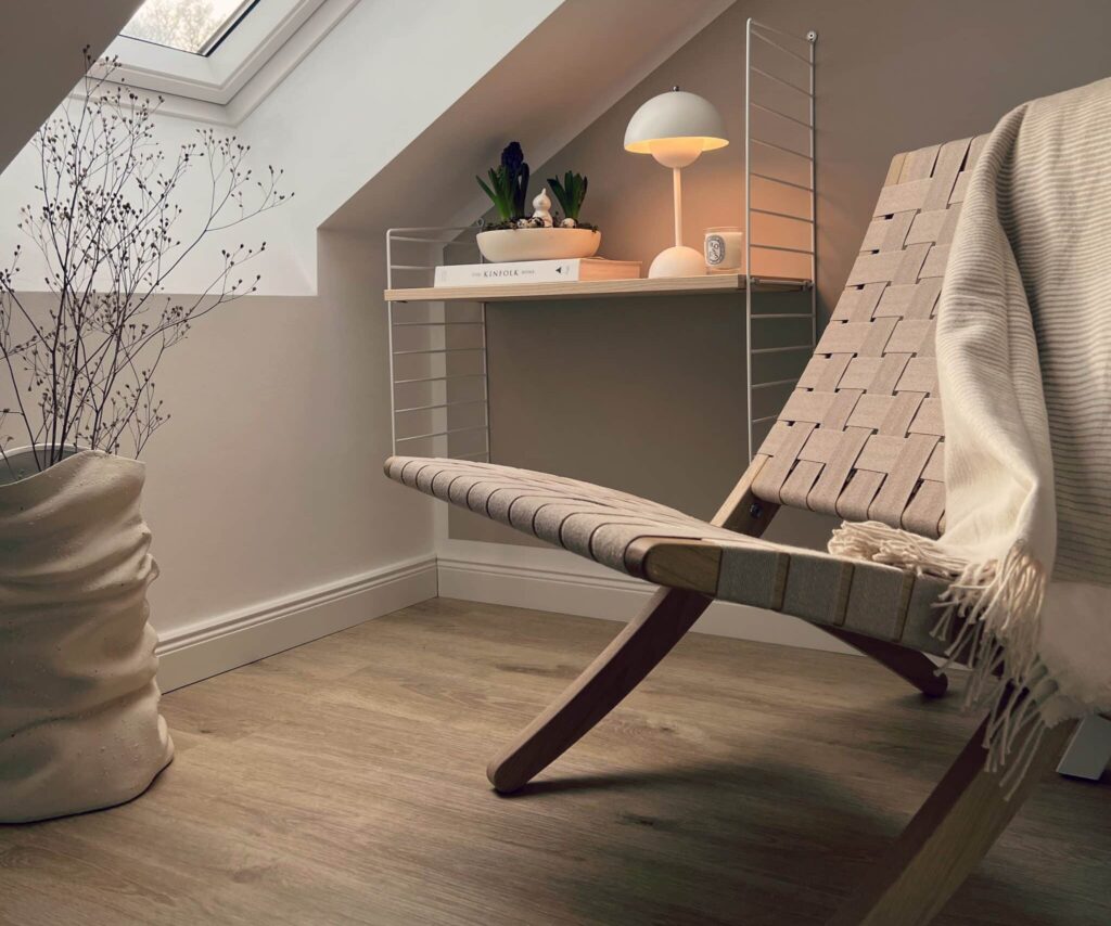 Vinylboden Schräg gestellter Sessel mit gewebtem Sitz und hellgrauer Decke in einem Raum mit Dachfenster und hellem Vinylboden.